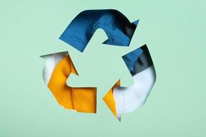 tweede hand, kleding bijdrage en recycling concept. kleurrijk kleren onder papier besnoeiing recycling symbool foto