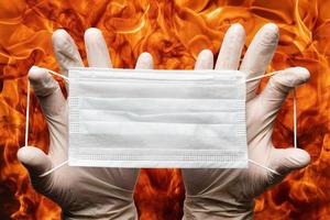 menselijk handen Holding veel ademhalings gezicht maskers in wit medisch handschoenen Aan achtergrond vlammen van sterk rood brand foto