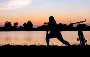 silhouet vrouw oefening in de buurt fiets Aan zonsondergang. foto