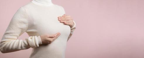 vrouw handen controle knobbeltjes Aan haar borst voor tekens van borst kanker Aan roze achtergrond. gezondheidszorg concept. foto