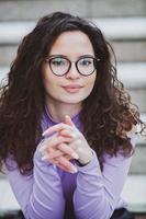 mooi jong vrouw met brunette gekruld haar, portret in oog bril genieten van de zon in de stad. foto