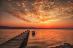 verbazingwekkend zonsondergang of zonsopkomst Bij een kust met houten pier en visvangst boot foto