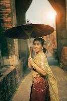 mooi Aziatisch vrouw vervelend Thais traditie kleren Holding bamboe paraplu staand in oud tempel Bij ayutthaya wereld erfgoed plaats van UNESCO centraal van Thailand foto