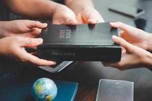 concept van christen ministerie. klein groepen bidden samen voor de christen missie. missie naar verspreiding de Evangelie en religie van Christendom in de omgeving van de wereld. handen Holding Bijbel Aan houten tafel. foto