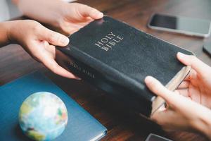 concept van christen ministerie. klein groepen bidden samen voor de christen missie. missie naar verspreiding de Evangelie en religie van Christendom in de omgeving van de wereld. handen Holding Bijbel Aan houten tafel. foto