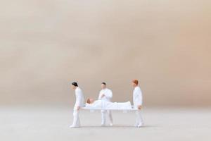 miniatuurartsen met verpleegsters die een patiënt op een brancard dragen, gezondheidszorgconcept
