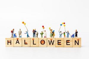 miniatuurmensen die ballons met houten blokken met tekst halloween op een witte achtergrond houden foto