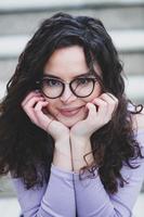 mooi jong vrouw met brunette gekruld haar, portret in oog bril genieten van de zon in de stad. foto