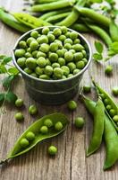 verse groene erwten in een kleine metalen emmer op oude houten achtergrond foto