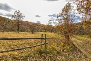 de landelijk herfst landschap met land weg en houten hek foto