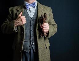 portret van heer in tweed pak Aan zwart achtergrond Holding leer handschoenen. wijnoogst stijl en retro mode. klassiek Engels heer. foto