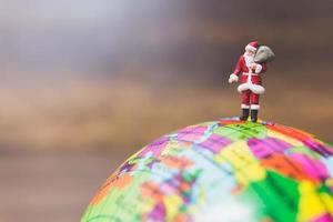 miniatuur kerstman met geschenken staande op een wereldbol foto