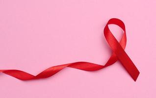 een zijde rood lint in de het formulier van een boog Aan een roze achtergrond, een symbool van de strijd tegen AIDS en een teken van solidariteit en ondersteuning foto