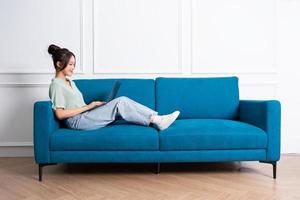 beeld van jong Aziatisch meisje zittend Aan sofa Bij huis foto