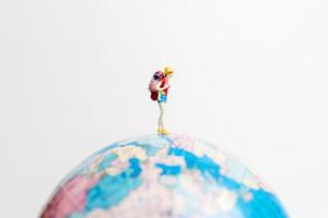 miniatuurpersoon die zich op een bol met een witte achtergrond, reisconcept bevindt foto