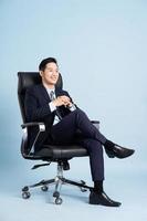 Aziatisch zakenman mannetje portret zittend Aan stoel en geïsoleerd Aan blauw achtergrond foto