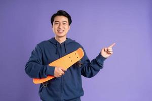 beeld van jong Aziatisch Mens spelen skateboard Aan Purper achtergrond foto