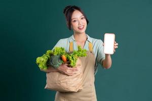 Aziatisch meisje portret Holding een zak van groenten Aan een groen achtergrond foto