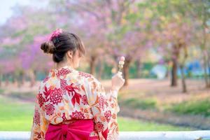 terug van Japans vrouw in traditioneel kimono jurk genieten reizen en Holding dango Bij brug in voorjaar festival. foto