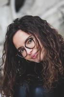 mooi jong vrouw met brunette gekruld haar, portret in oog bril genieten van de zon in de stad. foto