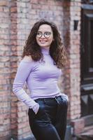 mooi jong vrouw met brunette gekruld haar, portret in oog bril genieten van de zon in de stad. foto