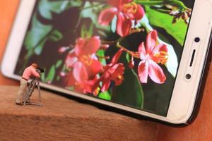 een miniatuur figuur van een videograaf filmen bloemen Aan een cel telefoon. foto