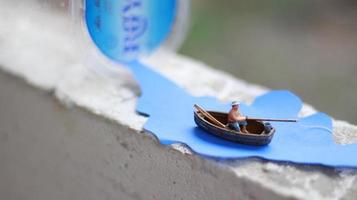 een miniatuur figuur van een visser visvangst in een rivier- gevisualiseerd Aan blauw papier uitsparingen. foto