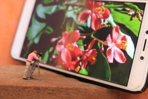 een miniatuur figuur van een videograaf filmen bloemen Aan een cel telefoon. foto