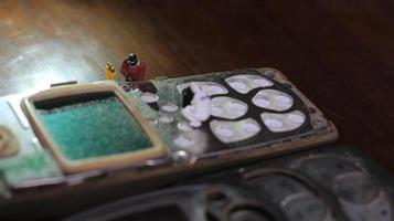 miniatuur figuur van een technicus repareren een oud gebroken cel telefoon. werken technicus concept. foto