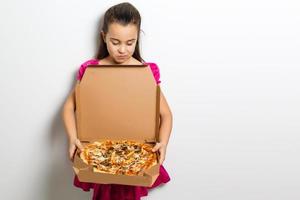 schattig weinig Indisch Aziatisch meisje kind aan het eten smakelijk pizza in doos. staand geïsoleerd over- wit achtergrond. foto