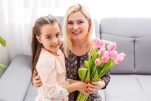 gelukkig moeder dag. kind dochter feliciteert moeders en geeft haar bloemen tulpen foto