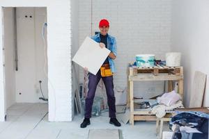 meester is installeren verdieping keramisch tegel in een kamer, drukken naar beneden en egaliseren, interieur afwerking van gebouwen van een leven huizen foto