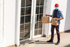 levering Mens Holding papier zak met voedsel Aan wit Ingang van huis achtergrond , voedsel levering Mens in beschermend masker foto