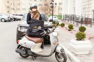 gemaskeerd vrouw leveren voedsel Aan een motorfiets foto