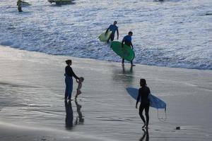 surfers krijgen klaar naar invoeren de water en wandelen met de bord langs de oever. foto