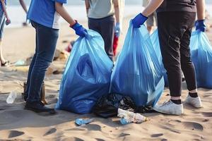 een groep van onherkenbaar mensen verzamelen vuilnis van de strand in blauw Tassen voor de probleem van plastic verontreiniging in de milieu foto