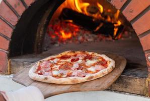 chef plaatsen pizza in steen oven foto