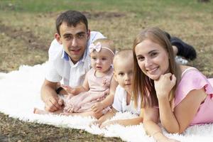 man en vrouw en hun weinig kinderen. familie portret in natuur. mam en vader zijn Holding een broer en zus in hun armen. jong familie met kinderen voor een wandelen. foto