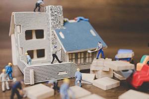miniatuurarbeiders die een huis op een houten achtergrond herstellen foto