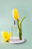 een transparant fles van vrouwen parfum of toilet water staat Aan een wit ronde marmeren podium met een voorjaar bloem. Product presentatie. maquette. foto