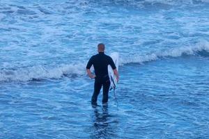 surfers krijgen klaar naar invoeren de water en wandelen met de bord langs de oever. foto