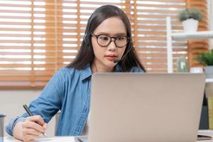 video telefoongesprek, vergadering conferentie via camera, gelukkig mooi Aziatisch jong vrouw, meisje zitten, slijtage draadloze koptelefoon studie online, gebruik makend van laptop computer, freelancer werkende.technologie, sociaal afstand. foto