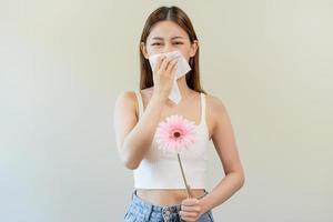 allergisch rhinitis symptoom van geur stuifmeel bloeiend, portret Aziatisch jong vrouw hand- in niezen, blazen vloeibaar neus- na geur, stinkend van bloeien bloem, Holding weg roze flora Aan wit achtergrond. foto