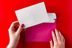 een felicitatie-envelop in de handen van een jonge vrouw op een rode achtergrond