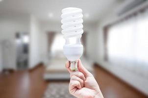 energie besparing concept, vrouw hand- Holding licht lamp Aan kamer huis achtergrond, ideeën licht lamp in de hand- foto