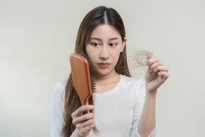 echt, bezorgd Aziatisch jong vrouw, meisje Holding borstel, tonen haar kam, haarborstel met lang verlies haar- probleem na poetsen, haar- vallen uit Aan haar hand- in leven kamer. Gezondheid zorg, schoonheid behandeling. foto