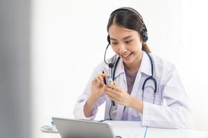 dokter of arts vervelend wit jas, stethoscoop gebruik makend van koptelefoon, overleg plegen Gezondheid door telehealth online voor sprekend video telefoontje overleg Aan tablet. telegeneeskunde door medisch voor afstand geduldig. foto