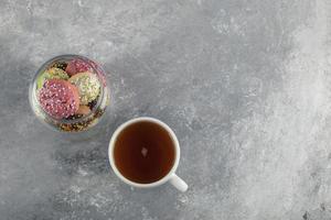 een glazen pot vol kleine kleurrijke donuts met een kop hete thee