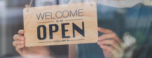 eigenaar bedrijf kleinhandel, Aziatisch jong vrouw hand- in draaien teken bord naar Open koffie winkel, vervelend gezicht masker beschermen naar pandemisch van coronavirus, heropenen op te slaan na dichtbij vergrendeling quarantaine in covid19. foto