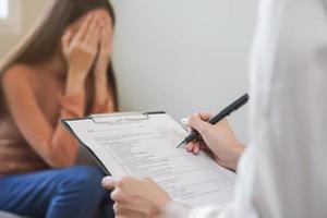 psychologie, depressie. verdrietig, lijden Aziatisch jong vrouw overleg plegen met psycholoog, psychiater terwijl geduldig begeleiding mentaal met dokter vrouw nemen aantekeningen Bij kliniek. bemoedigend, therapie. foto